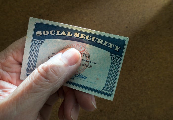 A person holding a Social Security card between their thumb and index finger. 