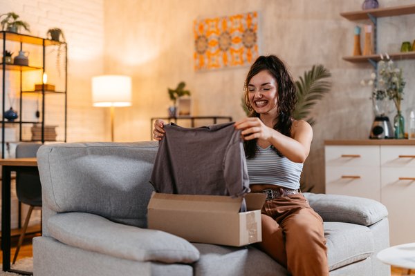 Smiling person holding up a shirt from inside a package.